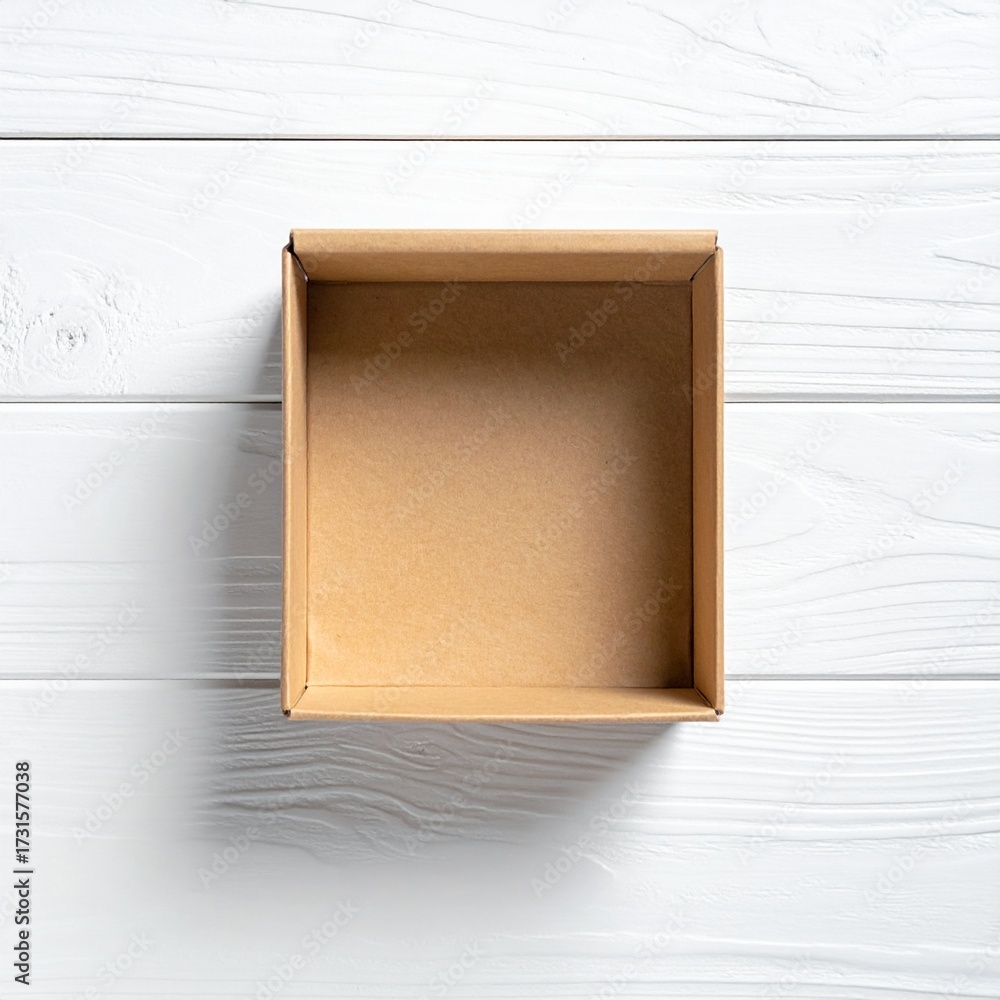 Fototapeta premium Top view of an empty square cardboard gift box on a white wooden surface. Flat lay composition for packaging mockup and design presentation
