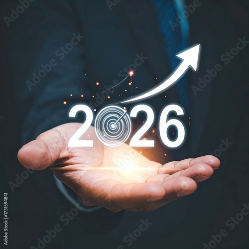 A businessman's hand holds a holographic projection of 2026, a target, and an upward arrow, signifying growth