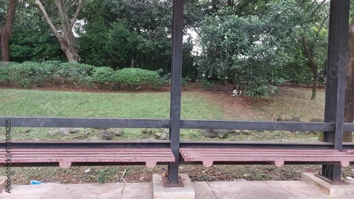 Video of an empty outdoor bus stop shelter featuring a long wooden bench and sturdy metal frame structure. 