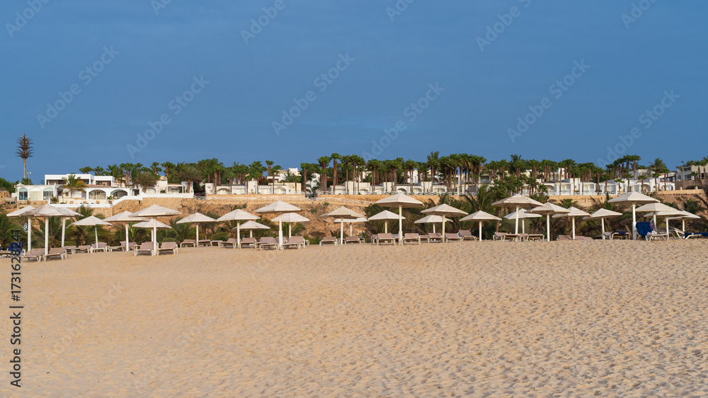 Obraz premium Beach scene with several umbrellas and beach chairs. The umbrellas are white and the chairs are beige. Scene is relaxed and peaceful, background luxury resort, Boa Vista,Cape verde