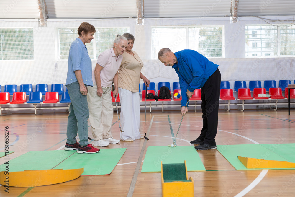 Obraz premium elderly group plays mini golf for competitions in the sprot hall. Kidult gaming in the gym. Active retirement community. dopamine hobbies. an active and healthy lifestyle in retirement. 