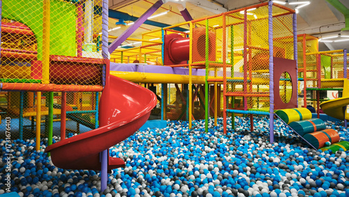 Colorful indoor playground with slides, climbing structures, and a ball pit full of blue, white, and black plastic balls, perfect for kids fun and birthday parties.