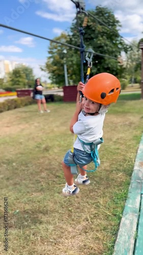 Little girl in helmet and safety gear sliding on a zip line in kids rope adventure park