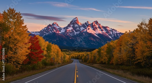 Scenic highway view leading towards mountain peaks with colorful autumn foliage under a clear sky