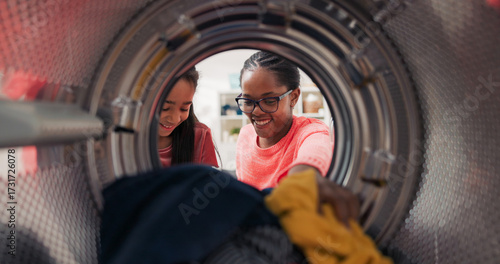 A cheerful daughter helps her mom with the laundry, holding clothes in her hands while the woman opens the washing machine drum, they enjoy spending time together.