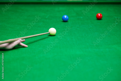 Close-up of snooker player aiming white cue ball on green table with red and blue balls, concept of precision, focus, and sports competition.
