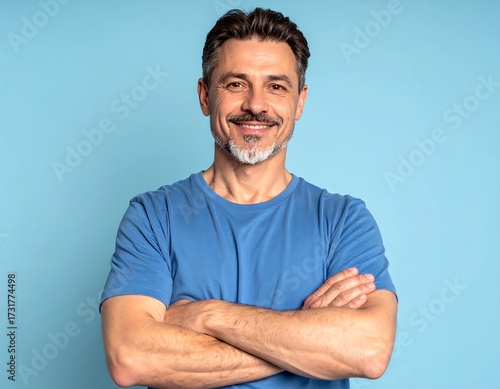 Smiling middle-aged man, arms crossed, against a light blue background.  Friendly, confident expression