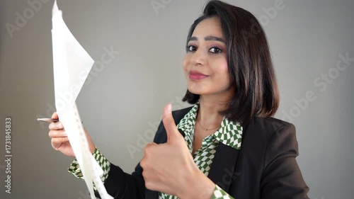 Closeup of happy successful businesswoman leader manager boss looking at camera hold documents paper and pen showing thumb up hand gesture approval agreement support, isolated over grey background.