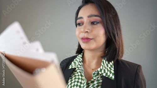 Closeup of happy successful busy young Indian businesswoman manager hold file reading checking documents information with focused concentrated face expression, isolated over grey background.