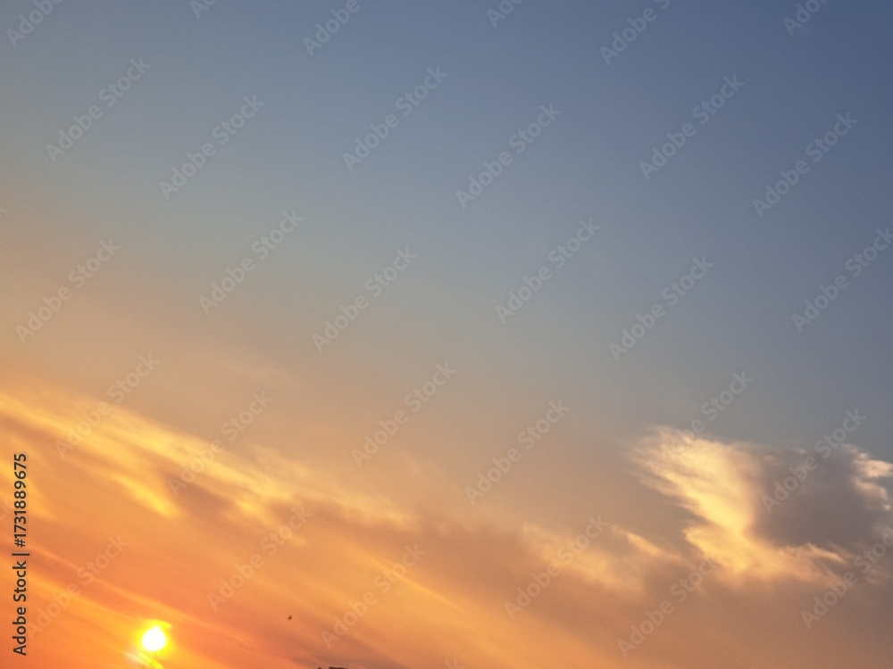Fototapeta premium Evening sunset with an orange blue sky – White and grey clouds illuminated by the last remaining rays of the bright orange evening sun, amidst a darkening blue sky.