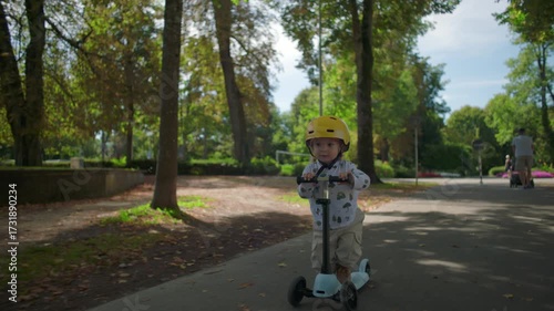 Wallpaper Mural Little child with yellow helmet riding scooter along tree-lined path in park, moving forward with curiosity and balance in natural outdoor environment Torontodigital.ca