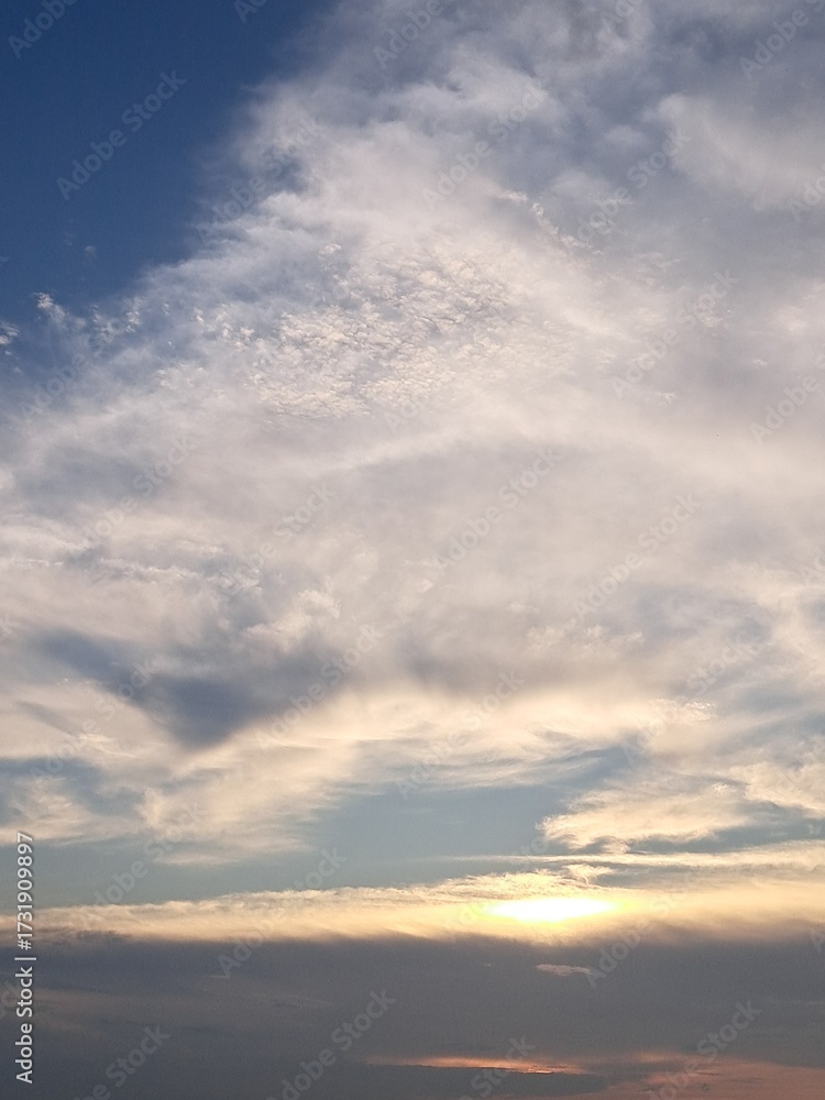 Fototapeta premium Evening sunset with a yellow blue sky – White and grey clouds illuminated by the last remaining rays of the bright yellow evening sun, amidst a darkening blue sky.