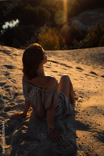 A girl in a gray dress walks on a sand dune at sunset in summer