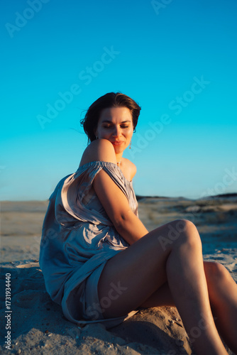 A girl in a gray dress walks on a sand dune at sunset in summer