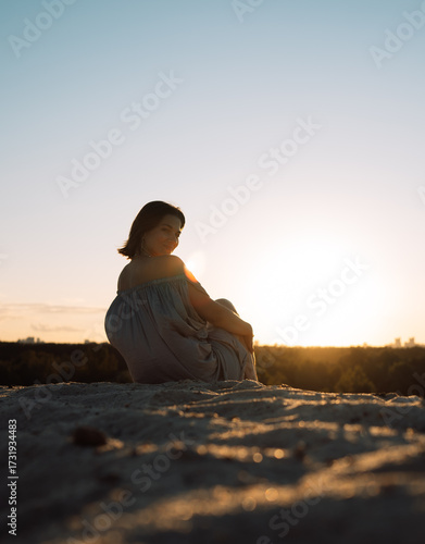 A girl in a gray dress walks on a sand dune at sunset in summer