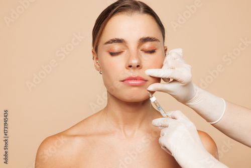 Fotografía Beautiful half naked topless young woman 20s with nude make up getting lip beauty injection isolated on plain beige color background studio portrait