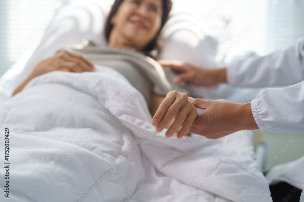 Obraz premium Doctor comforting smiling patient holding her hand in hospital bed