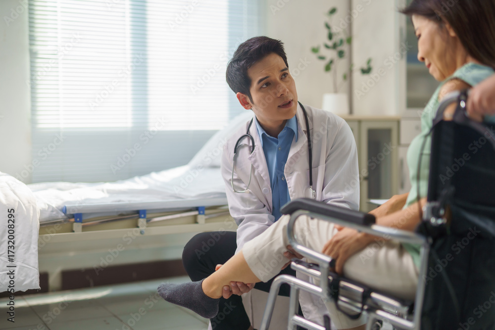 Fototapeta premium Doctor examining leg of senior patient in wheelchair at hospital