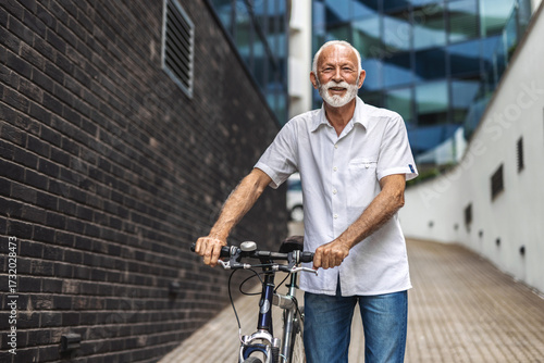 A cheerful senior man pushes his bicycle as he rushes to work. Mature men with commuting to work with his bicycle in city center.