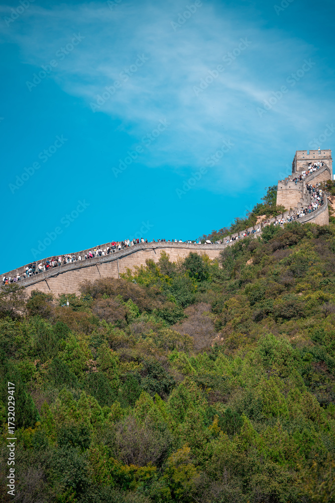 Fototapeta premium Ancient stone steps ascend a weathered, gray Great Wall winding through a lush, green landscape near Beijing, showcasing a historic defensive structure for travel and tours.