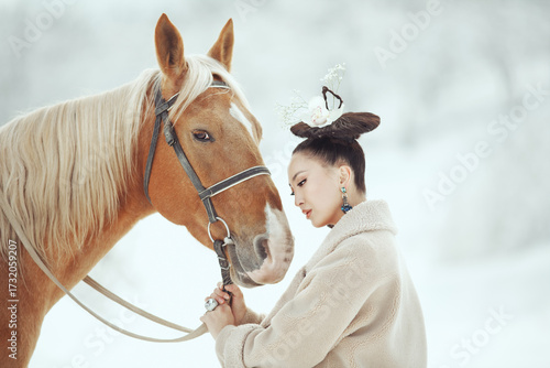 Young stylish asian woman in vintage outfit standing close to a brown horse