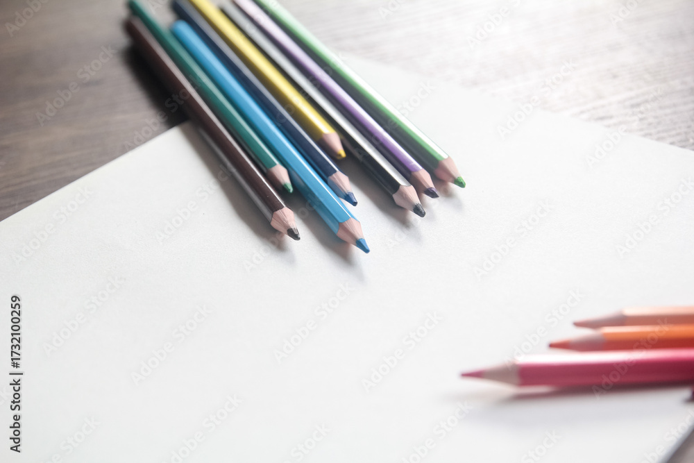 Fototapeta premium Group of colorful pencils diagonally aligned on a blank white sheet, ready for design or drawing with ample copy space.