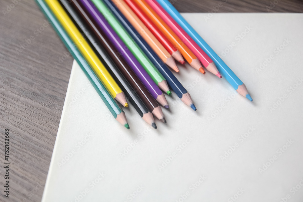 Fototapeta premium Close-up of a fan of vibrant colored pencils arranged on a plain white sheet of paper on a wooden desk.