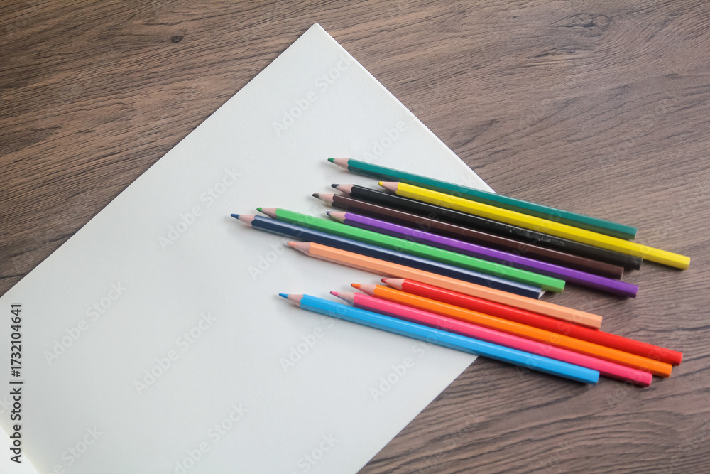 Obraz premium Close-up of a fan of vibrant colored pencils arranged on a plain white sheet of paper on a wooden desk.