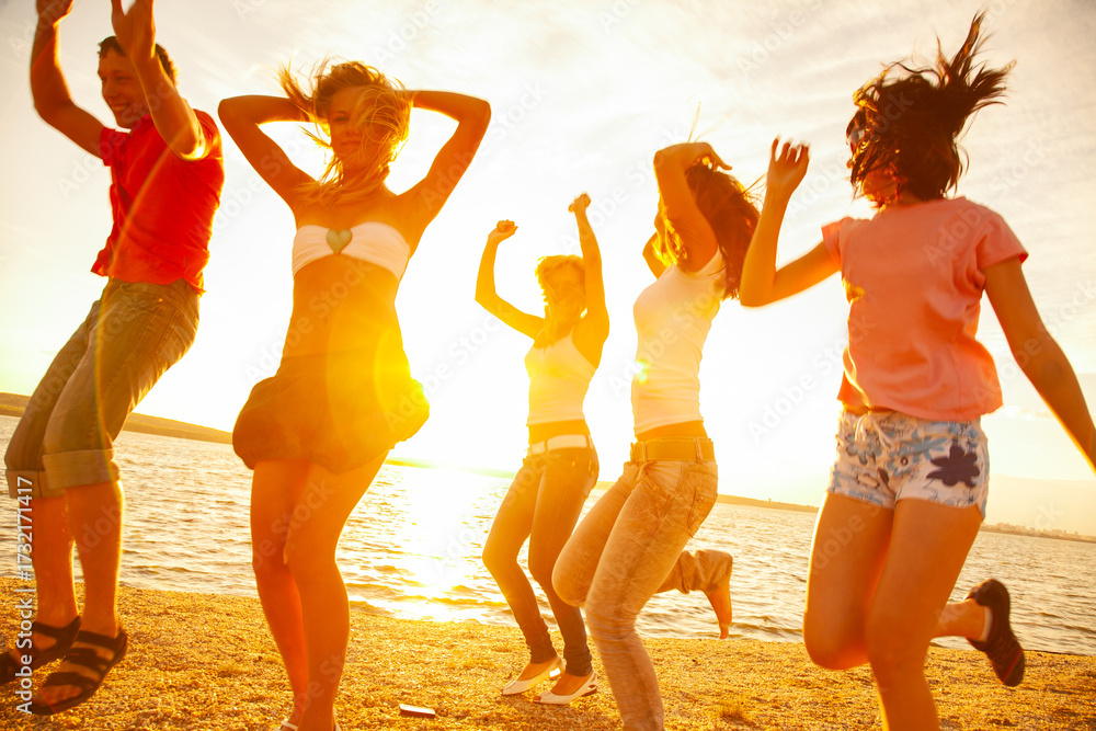 Fototapeta premium Young men and women dancing on the beach at sunset on a summer evening