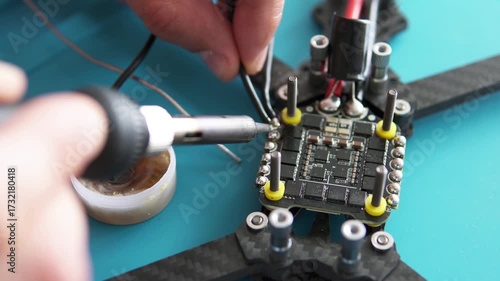 A specialist performs soldering on an FPV drone, attaching power and signal wires to its control board.