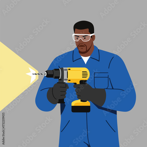 Worker using drill, wearing safety glasses and blue work clothes on a gray backdrop