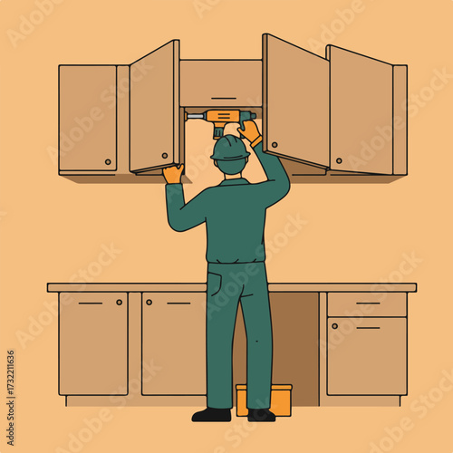 Repairman uses a drill to fix wood cabinets in kitchen, wearing green uniform