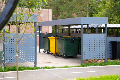Containers for waste sorting. A clean and organized waste management area features green and yellow recycling bins under a shelter