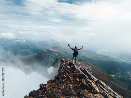 Man climber standing on mountain summit in Norway travel climbing vacations in Sunnmore Alps adventure trip outdoor healthy lifestyle, active traveler raised hands success harmony with nature freedom