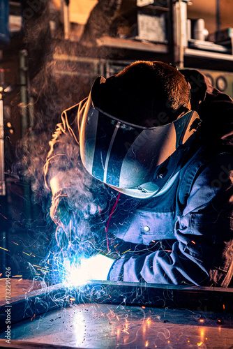 Industrial worker welding metal in workshop creating sparks and smoke