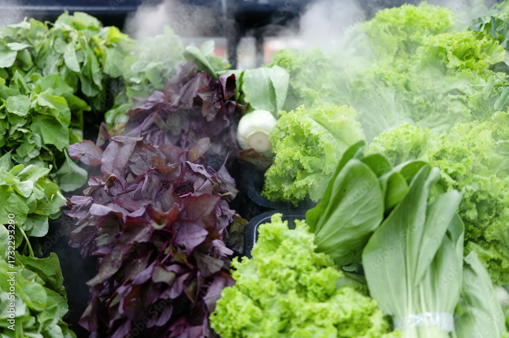 Φωτογραφία A variety of fresh green and purple leafy vegetables, including lettuce and amaranth, being kept cool by a misting system at a grocery store display