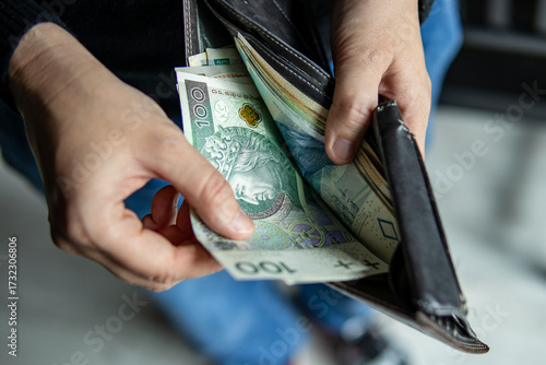 Close-up of hands pulling a 100 Polish zloty banknote from a wallet. Concept of cash transaction, finance, personal spending