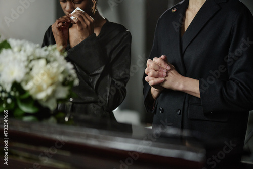Obraz na plátně Black woman and Caucasian woman standing at coffin, Black woman holding tissue n