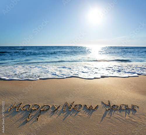 Happy New Year lettering on the sunny beach sand.