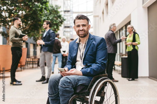 Portrait of smiling male business expert with physical disability sitting on wheelchair while holding smart phone at con
