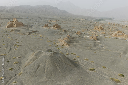 Aerial view of ancient ruins rise from the dusty earth, whispering tales of forgotten empires against a backdrop of hazy mountains, Subashi Ancient Town, Xinjiang, China.