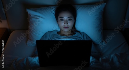 Woman working at night in bed with laptop in dim light. Working at night causes insomnia and sleep deprivation, affecting health.
