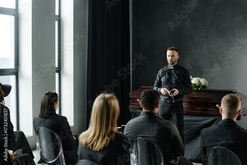 Fotografie Caucasian middle aged man standing and addressing group of adults during funeral