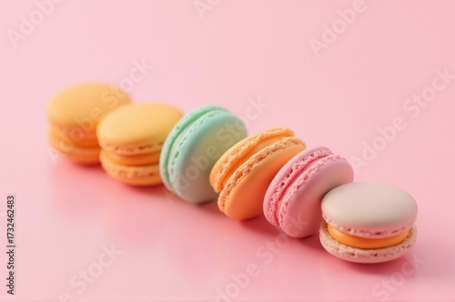 Six delightful macarons, each in a pastel hue, are arranged neatly against a soft pink backdrop. Their elegant shapes and vibrant colors create a visually pleasing display that is irresistible