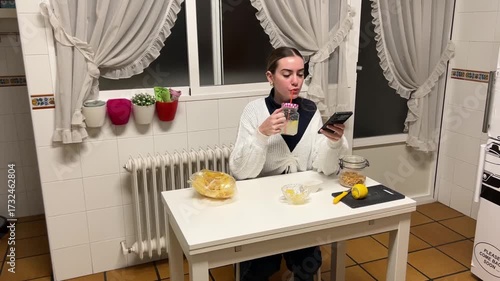 Teen girl drinking lemonade with a straw while looking at her phone during a casual kitchen moment