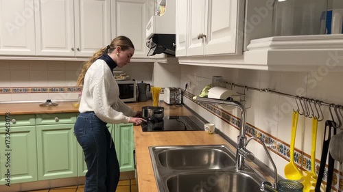 Teen girl placing pot on stove and turning on heat to boil water for pasta in home kitchen