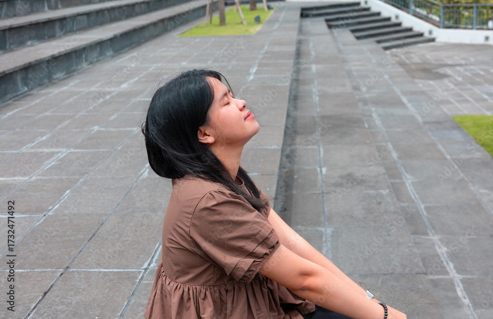 Fototapeta premium Young Asian woman smiling happily while relaxing in a green space. Beautiful lifestyle, enjoy life, green life, wellbeing concept, sustainable development. Stock photo