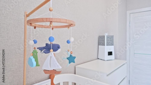 serene nursery with a wooden baby mobile featuring a whale, sailboat, starfish, and lighthouse. Soft blue tones, white crib, humidifier on dresser — calm, modern, nautical theme