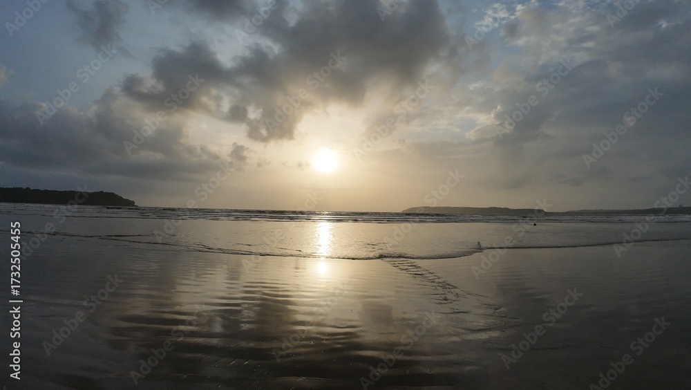 Naklejka premium Idyllic Coastal Sunrise with Gentle Waves, Dramatic Clouds, and Mirror-Like Reflections