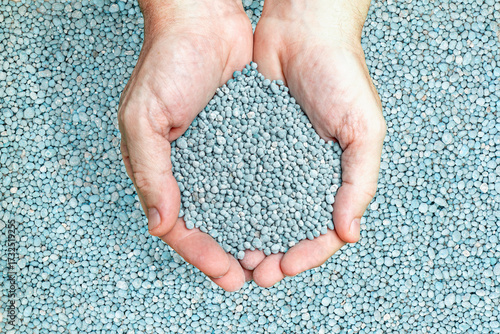 Hands holding blue granulated NPK chemical fertilizer for agriculture and gardening.